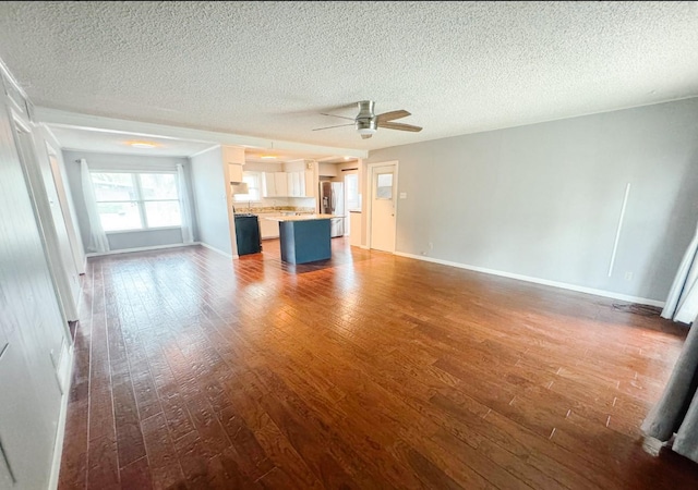 unfurnished living room featuring ceiling fan, dark wood-style flooring, and a textured ceiling