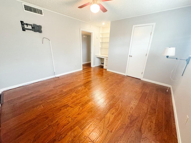 unfurnished bedroom featuring wood finished floors, a textured ceiling, ceiling fan, baseboards, and visible vents