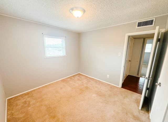 carpeted spare room featuring baseboards, visible vents, and a textured ceiling