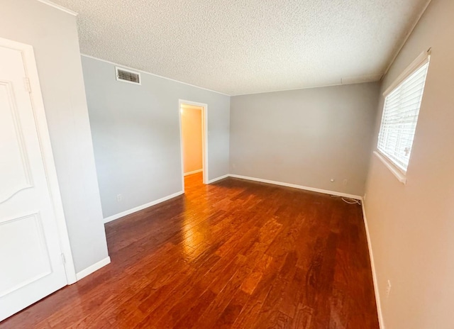 empty room featuring baseboards, wood finished floors, a textured ceiling, and visible vents
