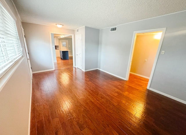 spare room with a textured ceiling, hardwood / wood-style floors, visible vents, and baseboards
