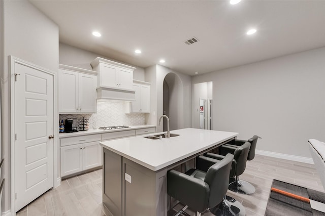 kitchen featuring stainless steel gas stovetop, an island with sink, backsplash, visible vents, and a sink