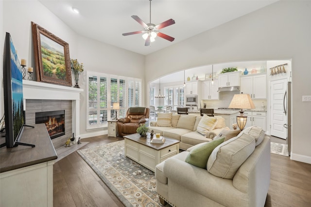 3204 Discovery Dr, Little Elm, TX 75068 - living area with a ceiling fan, a fireplace, a towering ceiling, baseboards, and dark wood-style flooring