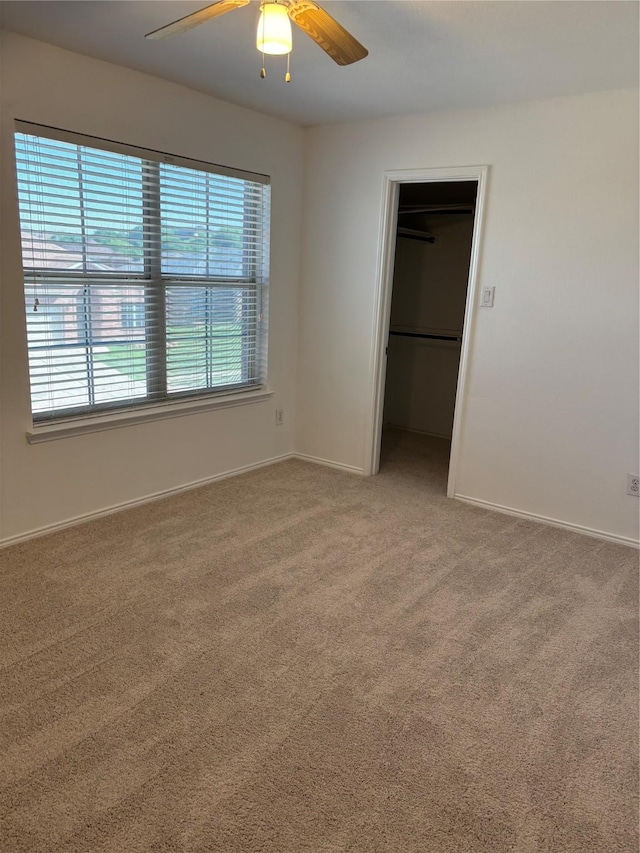 unfurnished bedroom featuring a spacious closet, light carpet, a closet, baseboards, and ceiling fan