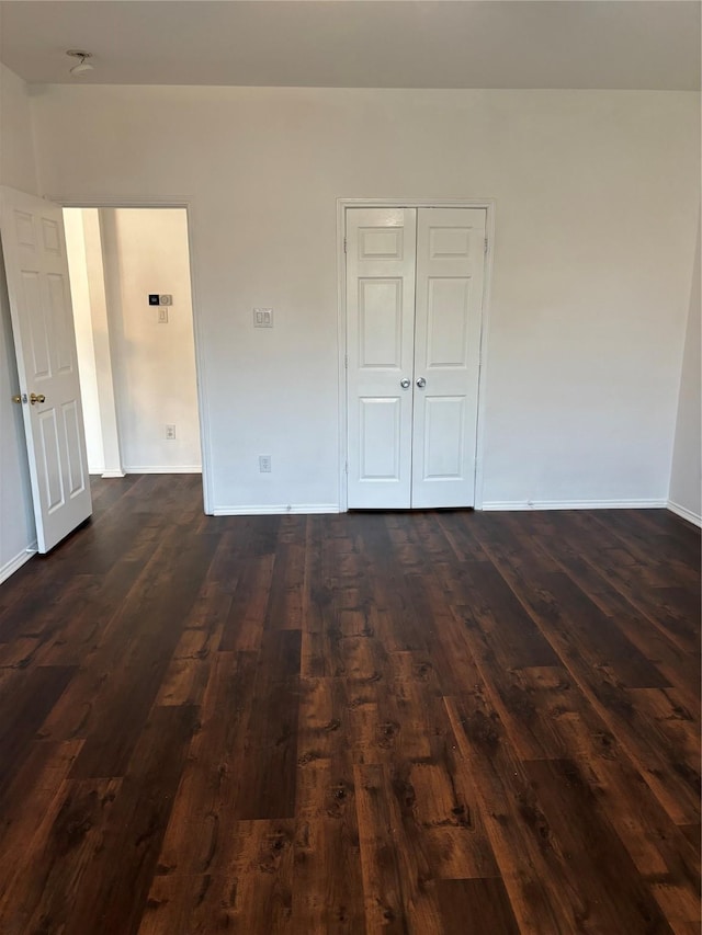 unfurnished bedroom with baseboards, dark wood-style floors, and a closet