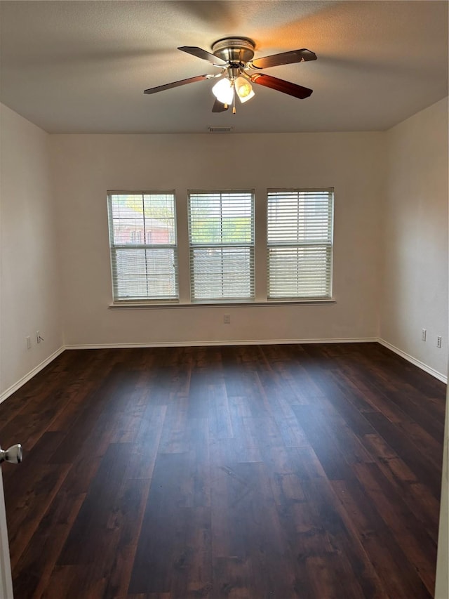 spare room featuring baseboards, visible vents, a ceiling fan, and dark wood-style floors