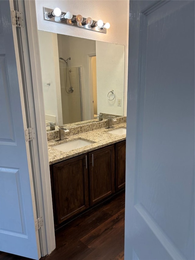 bathroom featuring walk in shower, wood finished floors, a sink, and double vanity