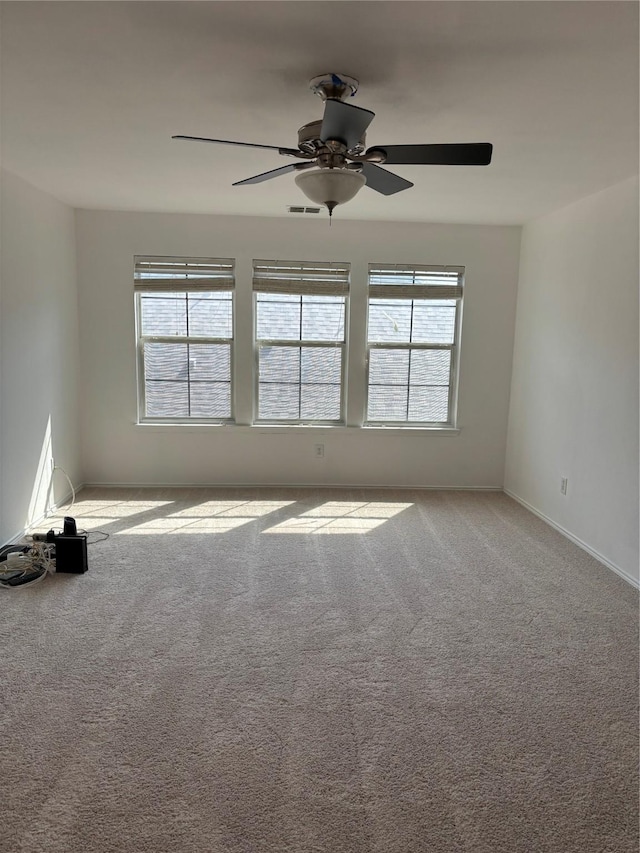 carpeted empty room featuring visible vents, a ceiling fan, and baseboards
