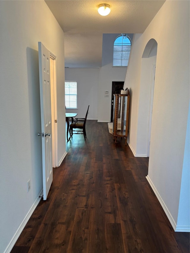 corridor with baseboards, dark wood-style floors, and arched walkways