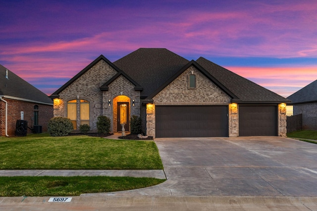 french country inspired facade with a garage, a lawn, brick siding, and driveway