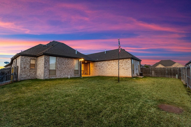rear view of property featuring brick siding, a lawn, a shingled roof, and a fenced backyard