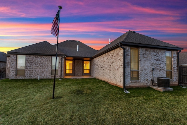 back of property at dusk with fence, a lawn, and brick siding