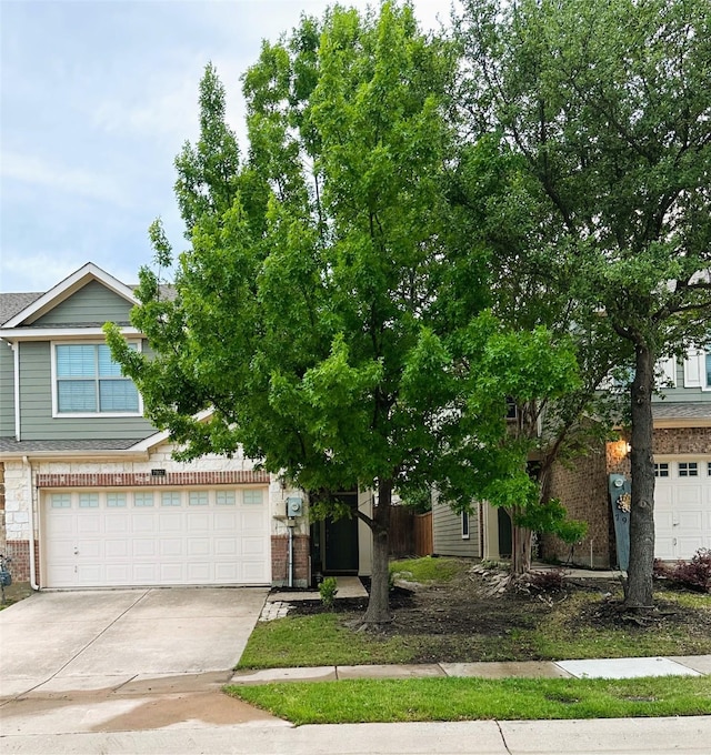 view of property hidden behind natural elements featuring concrete driveway, an attached garage, and brick siding