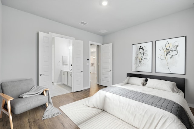 bedroom featuring baseboards, visible vents, wood finished floors, and ensuite bath