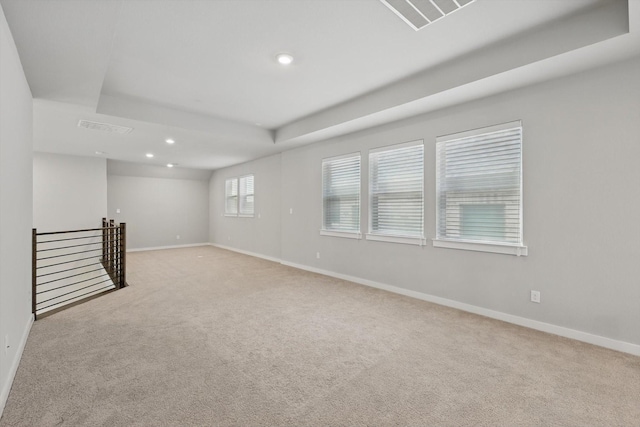 empty room featuring a raised ceiling, recessed lighting, baseboards, and light carpet