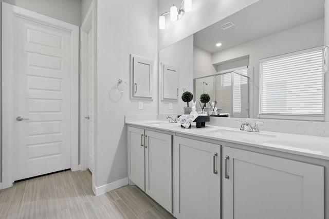 full bathroom with a stall shower, double vanity, a sink, and baseboards