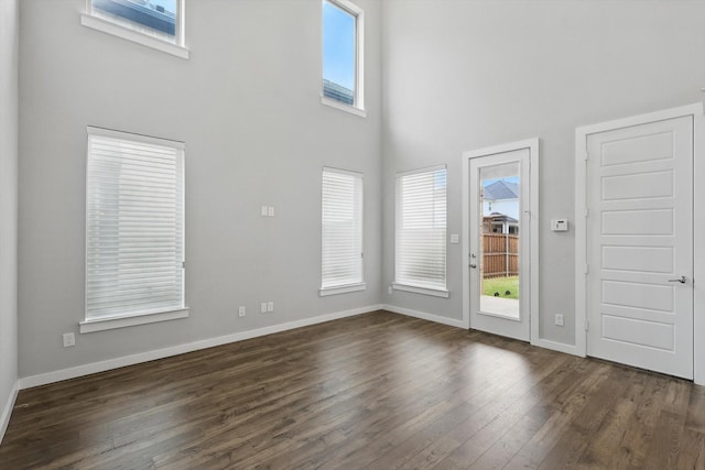 unfurnished living room featuring baseboards, a high ceiling, and dark wood-style flooring