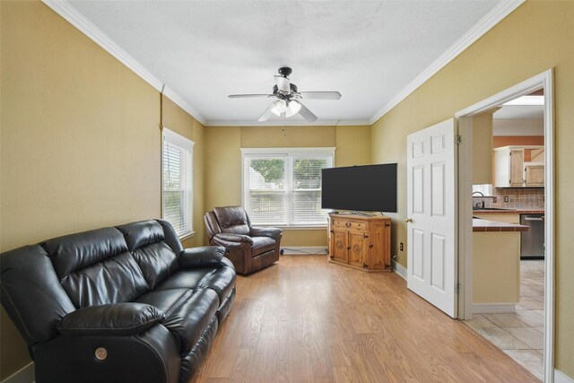 living area featuring light wood finished floors, a ceiling fan, baseboards, and crown molding