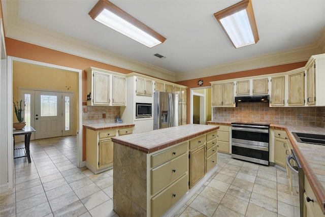 kitchen featuring tile counters, under cabinet range hood, stainless steel appliances, backsplash, and visible vents