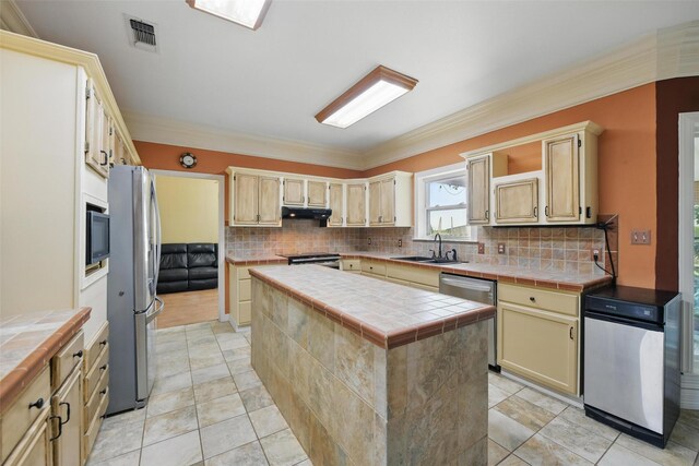 kitchen featuring a sink, tile countertops, stainless steel appliances, under cabinet range hood, and visible vents