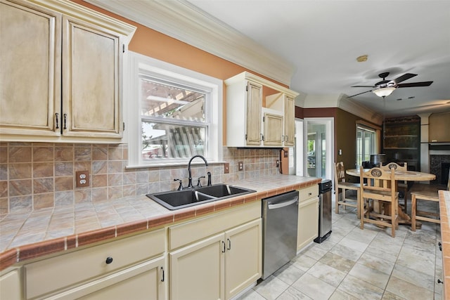 kitchen with tile countertops, stainless steel dishwasher, ornamental molding, a sink, and decorative backsplash