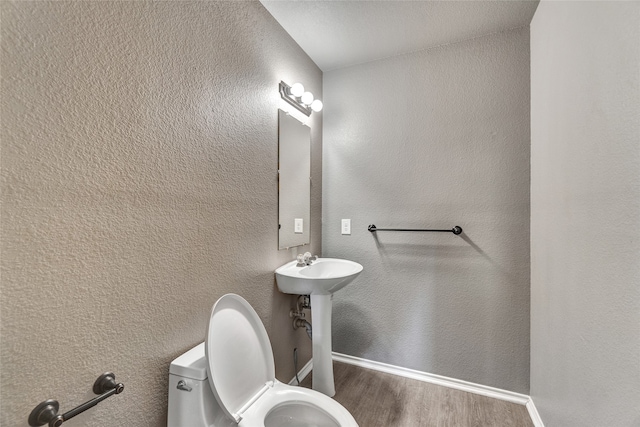 bathroom featuring baseboards, wood finished floors, and toilet