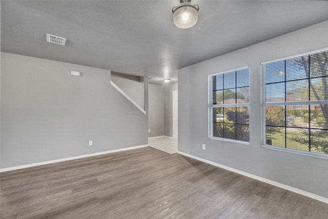 empty room featuring baseboards, wood finished floors, visible vents, and a healthy amount of sunlight