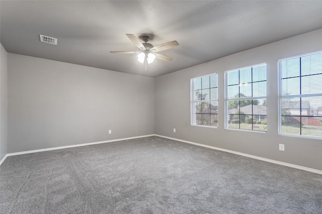 carpeted spare room featuring a wealth of natural light, a ceiling fan, baseboards, and visible vents