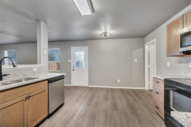 kitchen with light stone counters, a sink, a textured ceiling, light wood-type flooring, and stainless steel appliances