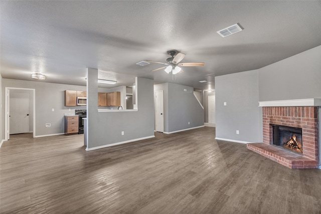 unfurnished living room featuring dark wood-style flooring, baseboards, visible vents, a brick fireplace, and ceiling fan