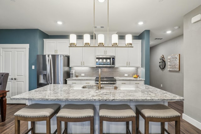 kitchen featuring dark wood-style floors, a sink, tasteful backsplash, a breakfast bar, and appliances with stainless steel finishes