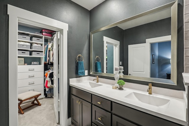 full bath featuring double vanity, a textured wall, a spacious closet, and a sink