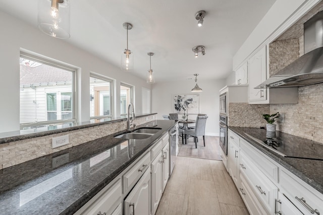 kitchen with wall chimney range hood, a sink, decorative backsplash, stainless steel appliances, and white cabinetry