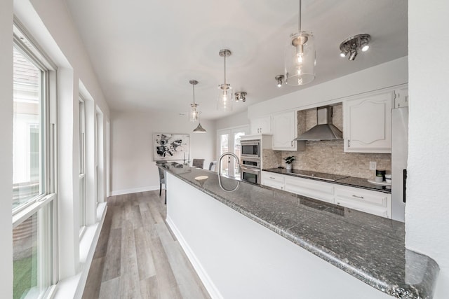 kitchen with decorative backsplash, stainless steel appliances, light wood finished floors, white cabinets, and wall chimney exhaust hood