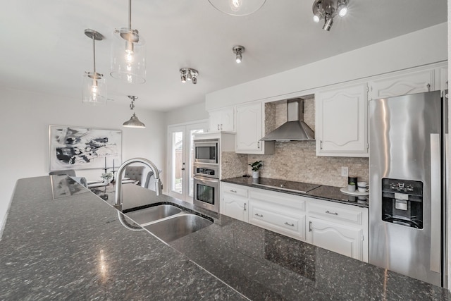 kitchen with wall chimney range hood, a sink, decorative backsplash, stainless steel appliances, and white cabinetry