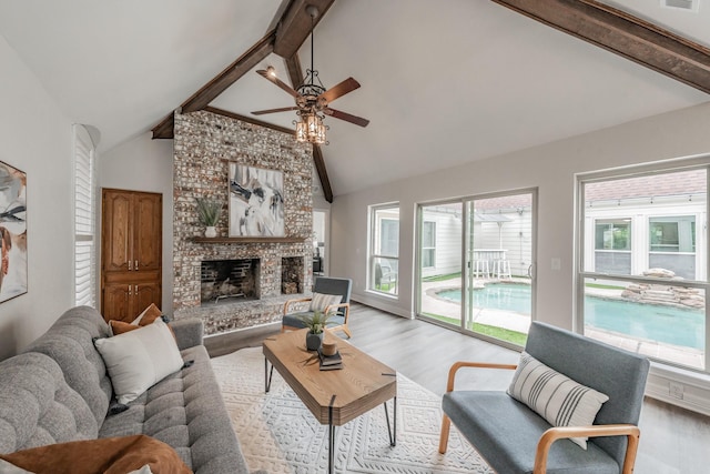 living area with high vaulted ceiling, a ceiling fan, light wood-type flooring, beamed ceiling, and a fireplace