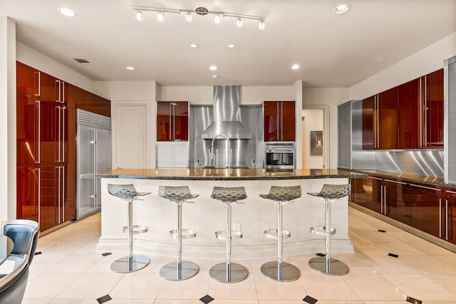 5608 Stone Cliff Ct, Dallas, TX 75287 - kitchen with stainless steel appliances, wall chimney range hood, reddish brown cabinets, modern cabinets, and a kitchen bar