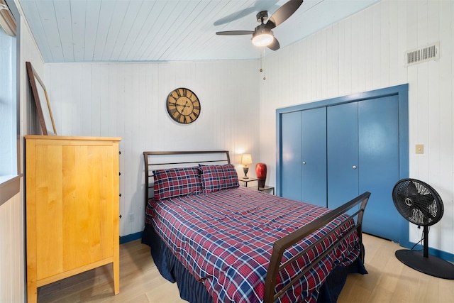 bedroom with visible vents, wood finished floors, wood walls, a closet, and ceiling fan