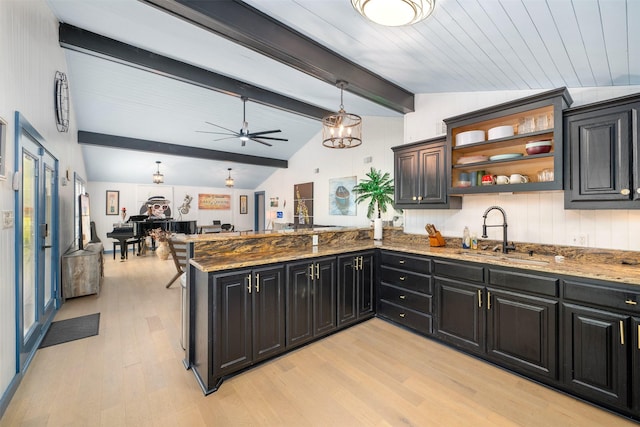 kitchen with lofted ceiling with beams, a sink, dark stone counters, open floor plan, and light wood-style floors
