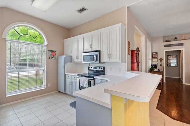 kitchen with a peninsula, baseboards, appliances with stainless steel finishes, light countertops, and light tile patterned floors
