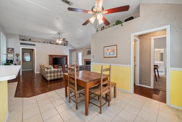 dining space with visible vents, lofted ceiling, ceiling fan, a fireplace, and light tile patterned floors