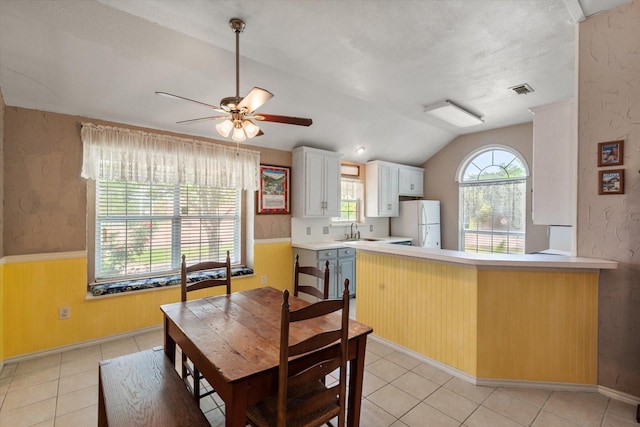 dining area featuring light tile patterned flooring, lofted ceiling, ceiling fan, and wainscoting