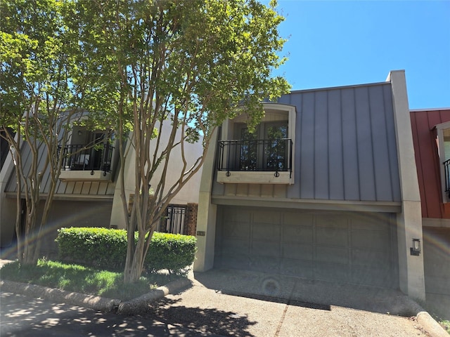 view of front of property featuring a garage, a balcony, a standing seam roof, driveway, and metal roof