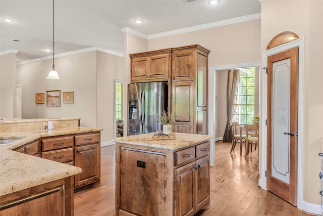 kitchen with a sink, brown cabinets, light stone counters, stainless steel refrigerator with ice dispenser, and a kitchen island