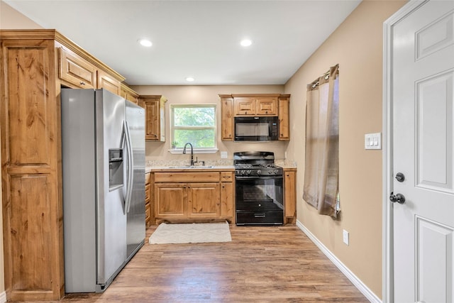 kitchen featuring a sink, black appliances, light wood-style flooring, baseboards, and recessed lighting