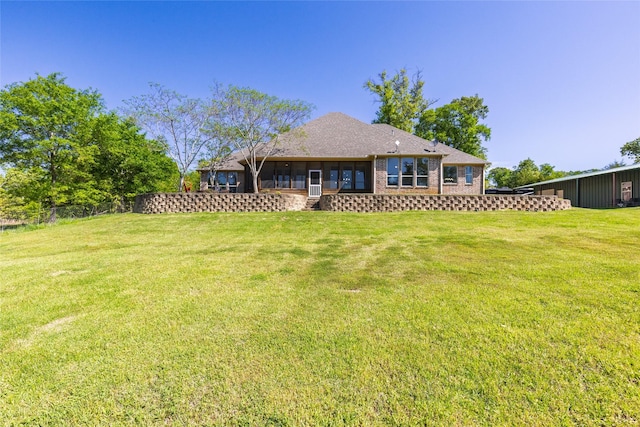 back of house with brick siding, a lawn, a shingled roof, and a sunroom