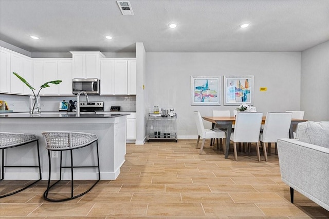 kitchen with dark countertops, tasteful backsplash, a breakfast bar area, stainless steel appliances, and visible vents