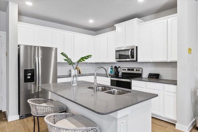 kitchen with light wood finished floors, stainless steel appliances, a sink, dark countertops, and backsplash