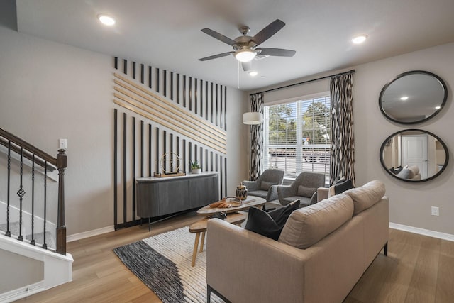 living area with wood finished floors, a ceiling fan, baseboards, and stairway