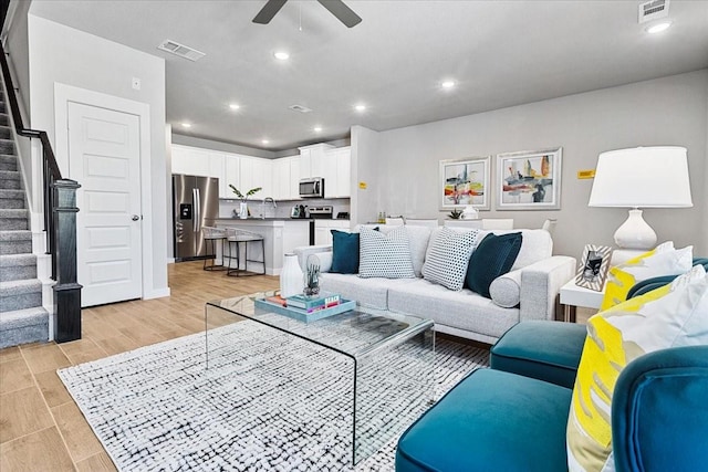 living room featuring a ceiling fan, stairs, visible vents, and light wood-style floors